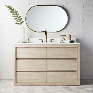 Modern single flat panel bathroom vanity with a light wood finish and white countertop, paired with a round mirror and gold fixtures.