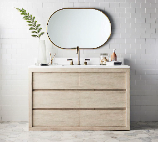 Modern single flat panel bathroom vanity with a light wood finish and white countertop, paired with a round mirror and gold fixtures.