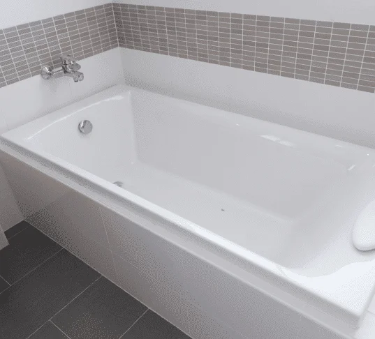 Clean white bathtub with mosaic tile surround and dark floor tiles. Bathtub Installation Cost.