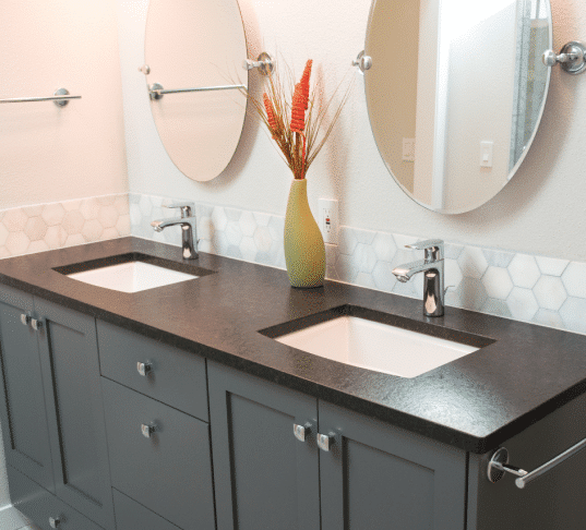 Double vanity with gray cabinets, dark countertops, and round mirrors. Vanity Installation Cost.