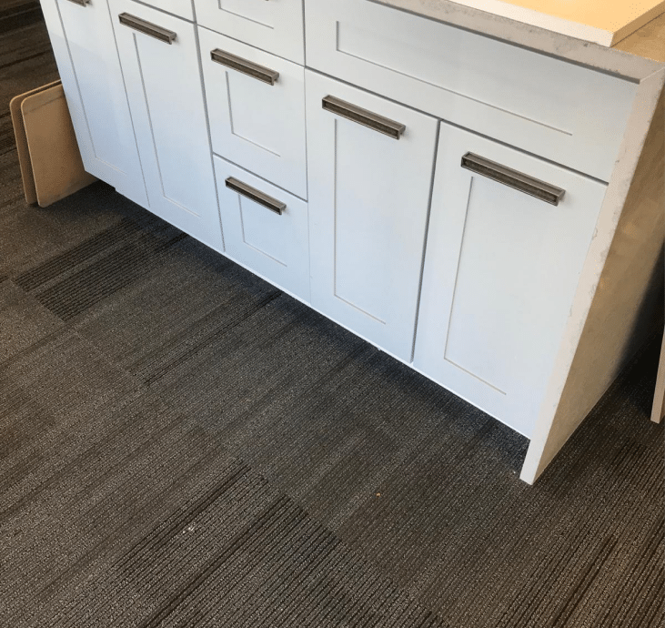 Close-up of white cabinetry with sleek metal handles on display, set against a dark carpeted floor in a cabinet showroom.