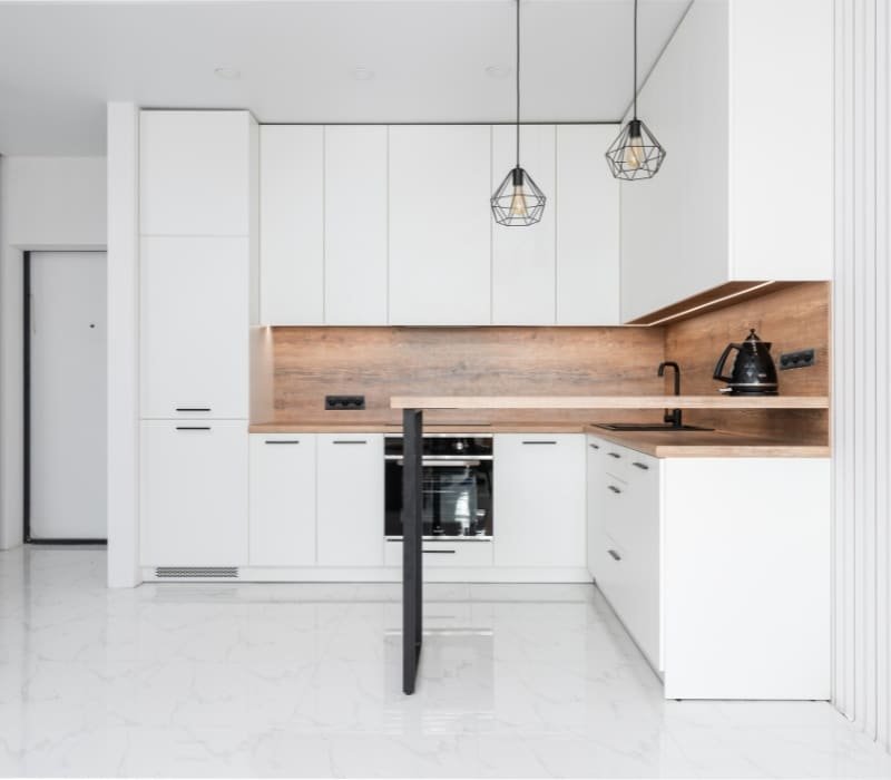 Modern minimalist kitchen design featuring white cabinets, a wooden backsplash, and elegant pendant lights, displayed in a Vancouver kitchen showroom.