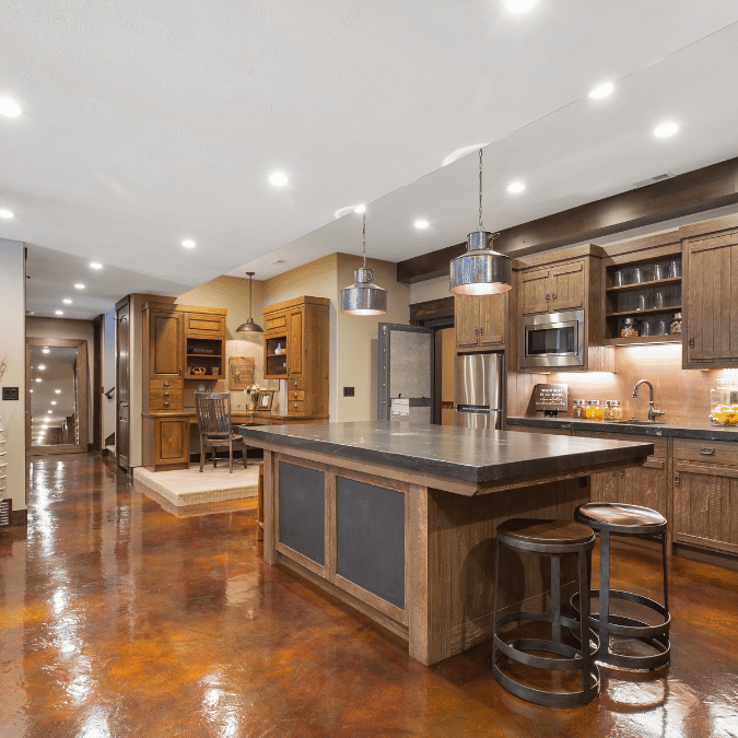 Modern basement kitchen with wooden cabinets, large island, and polished concrete flooring – highlighting basement renovation cost.