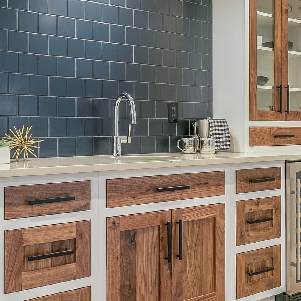 Modern kitchen featuring a navy tile backsplash, white quartz countertop, and natural wood cabinets with black handles.