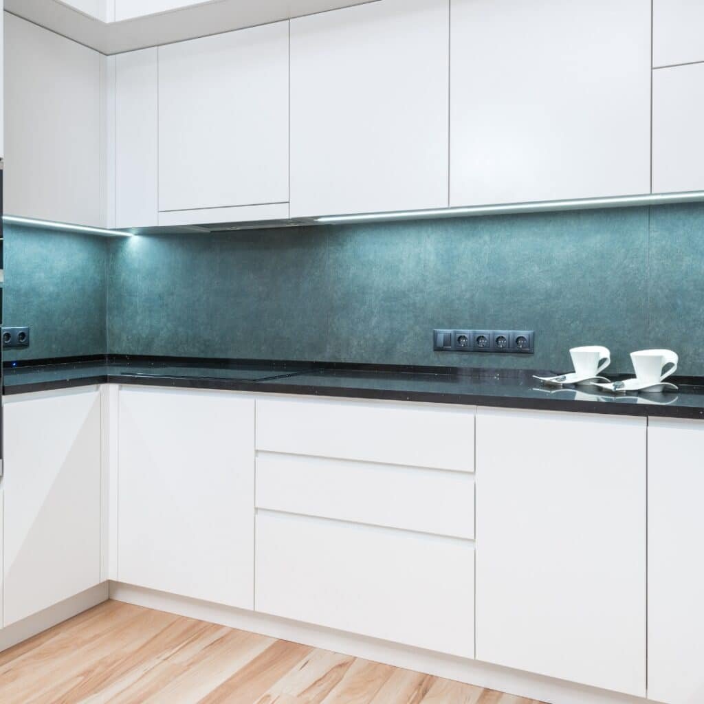 Modern kitchen with black countertops, green textured backsplash, and minimalist white cabinets under soft LED lighting.