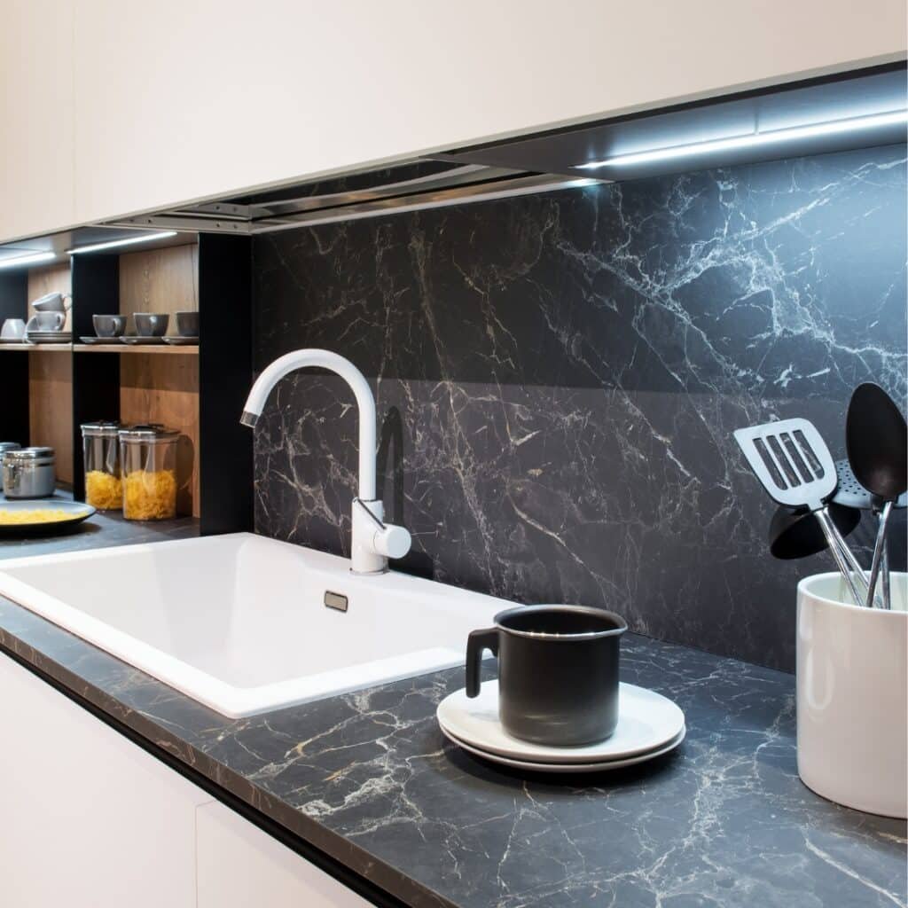 Modern kitchen with black marble countertops, matching marble backsplash, a white sink, and minimalist white cabinetry.