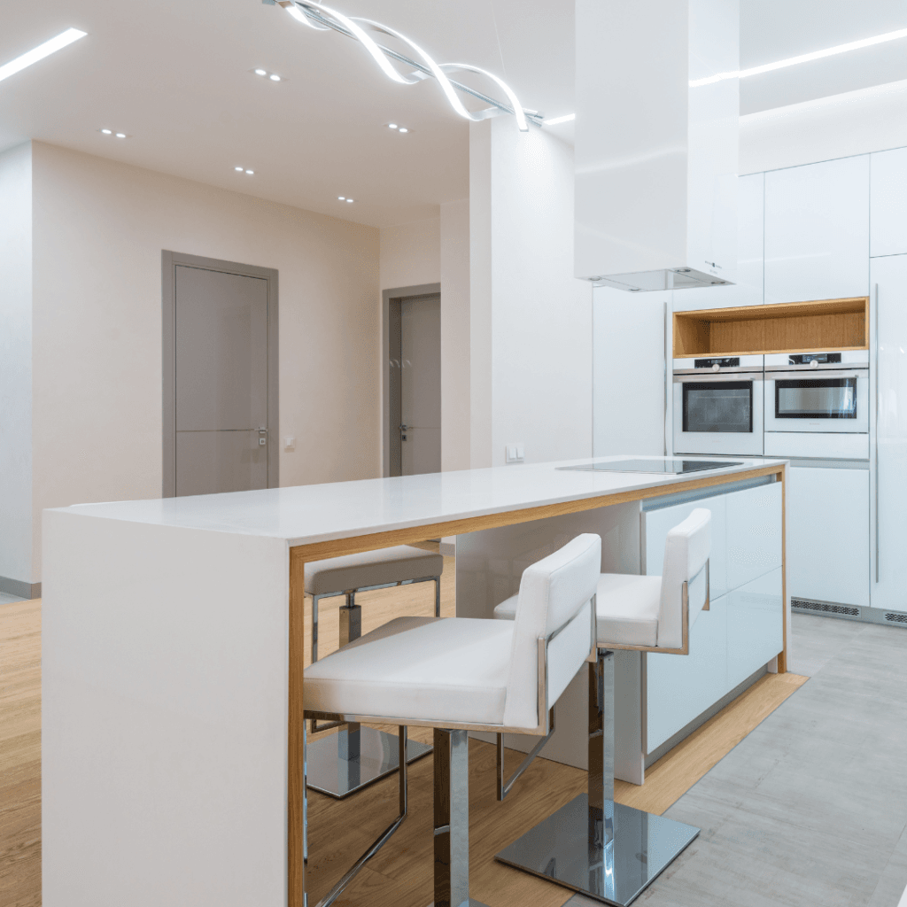 Modern kitchen with white cabinets, sleek countertops, wood accents, and chrome bar stools.