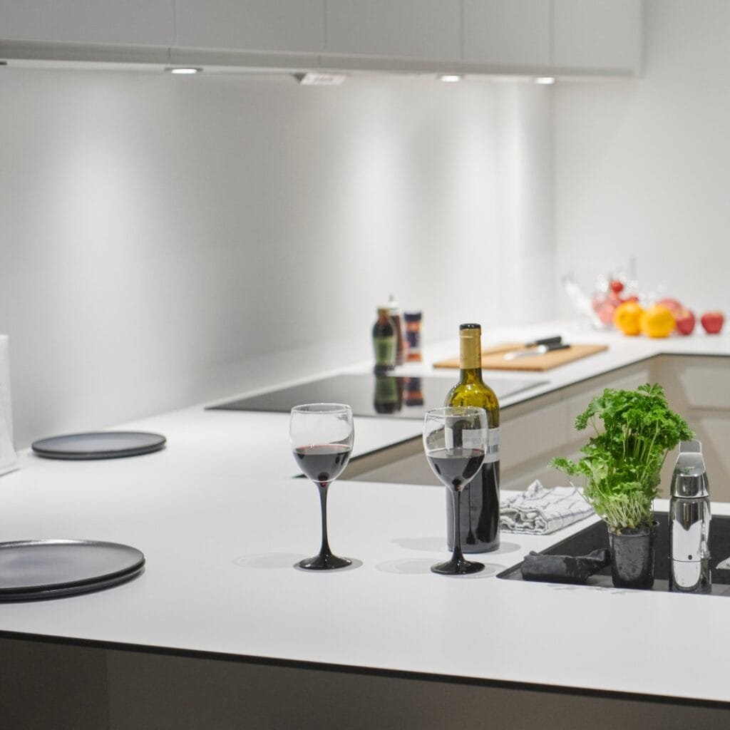 Modern kitchen with white countertops, minimalistic design, wine glasses, and fresh herbs.