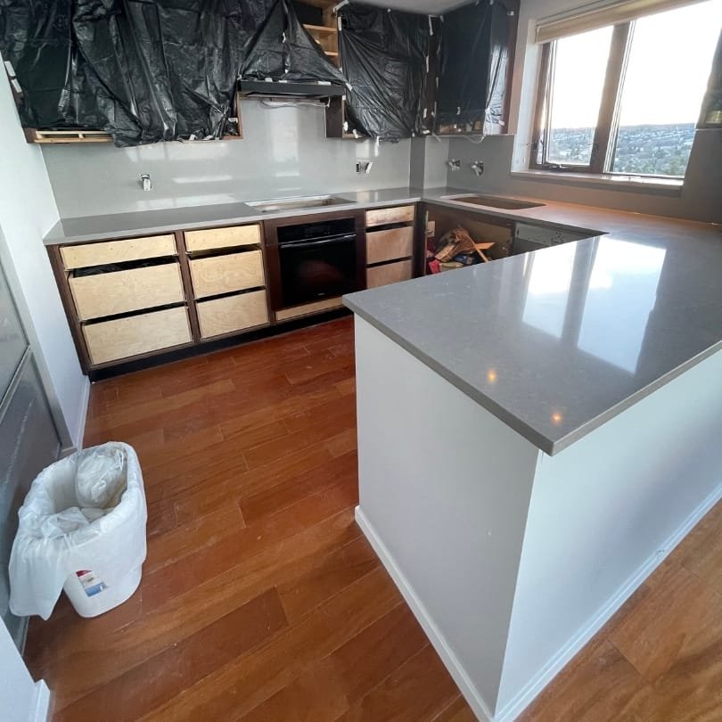 Kitchen remodeling in progress with uncovered cabinets, quartz countertops, and hardwood flooring.