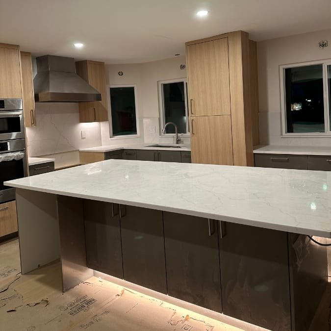 Modern kitchen remodel with light wood cabinets, a large white marble island, and stainless steel appliances.