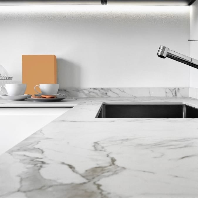 Minimalist kitchen with a marble countertop, stainless steel sink, and a simple backsplash.