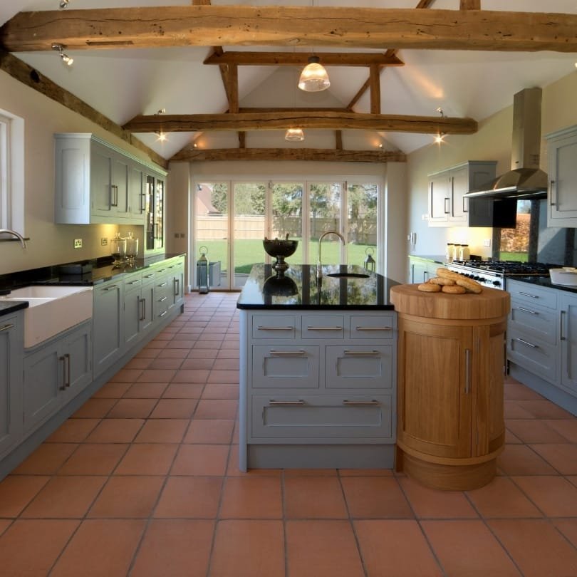 Earthy farmhouse kitchen with exposed beams, blue cabinetry, and terracotta tiles – ideal for kitchen renovation ideas in Vancouver.